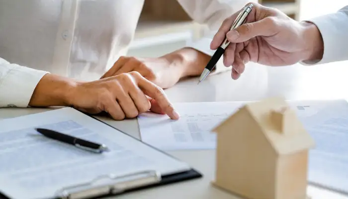 دو اقا در حال بررسی قرار داد ملکی در کنار یک ماکت چوبی خانه