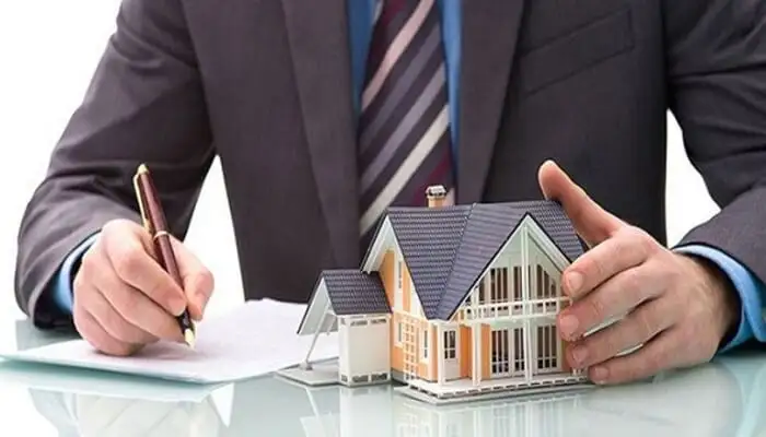 یک وکیل در حال امضا کردن قرار داد در کنار یک ماکت چوبی خانه ویلایی