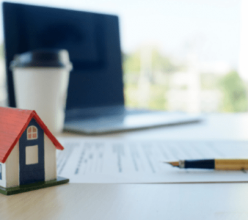 ماکت خانه در کنار لپ تاپ و خودکار روی میز