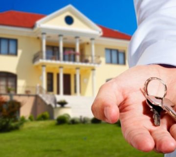 یک مرد کلید به دست که در پشت سر خود یک ویلا وجود دارد