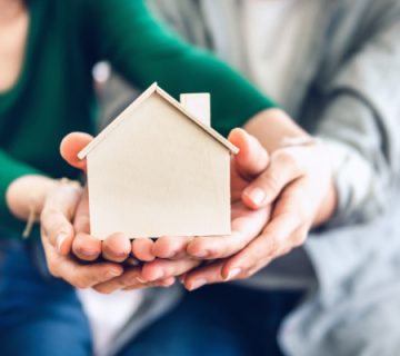 یک زن و شوهر که در دستان خود ماکت چوبی خانه دارند.