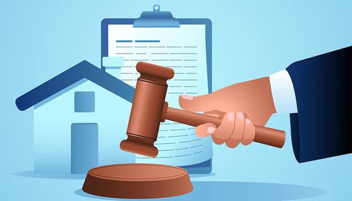 یک شخص در حال زدن چکش عدالت در کنار ماکت خانه