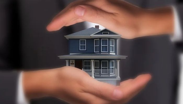 یک شخص که در میان دستان خود یک ماکت خانه را نگه داشته است.